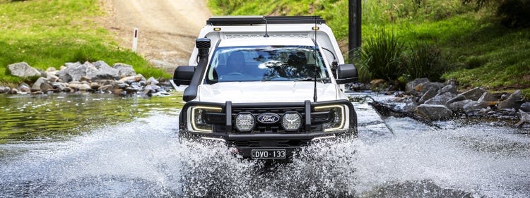 Front view of a Ford Ranger Super Duty fitted with an ARB bull bar, Intensity driving lights, snorkel, roof rack and canopy, crossing a shallow waterway.